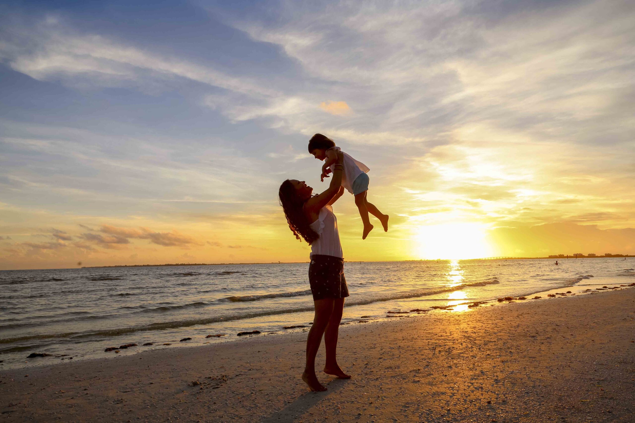 mother tossing child at sunset