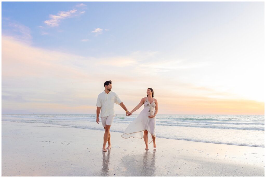 expecting couple holding hands down beach