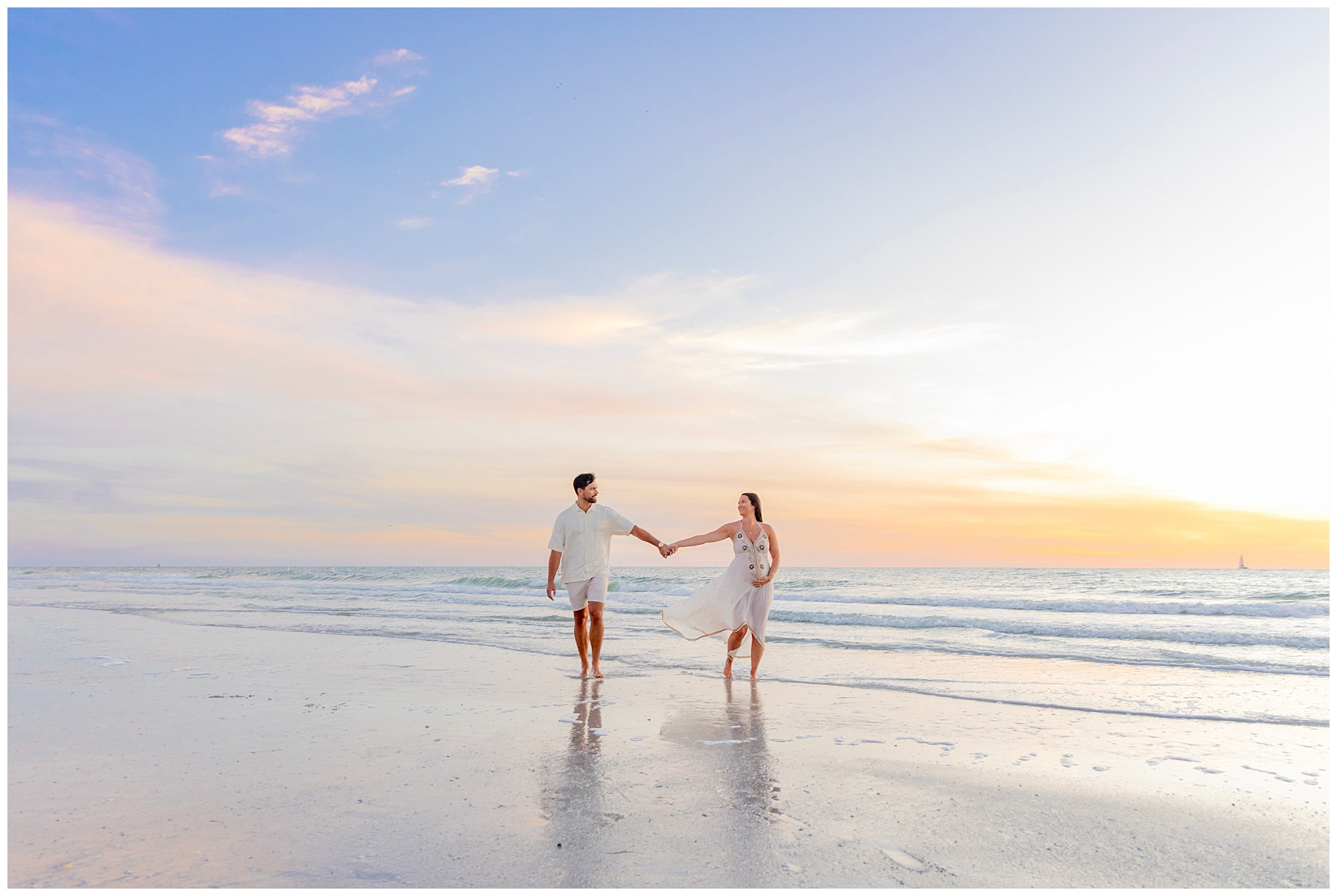 expecting couple holding hands down beach at sunset