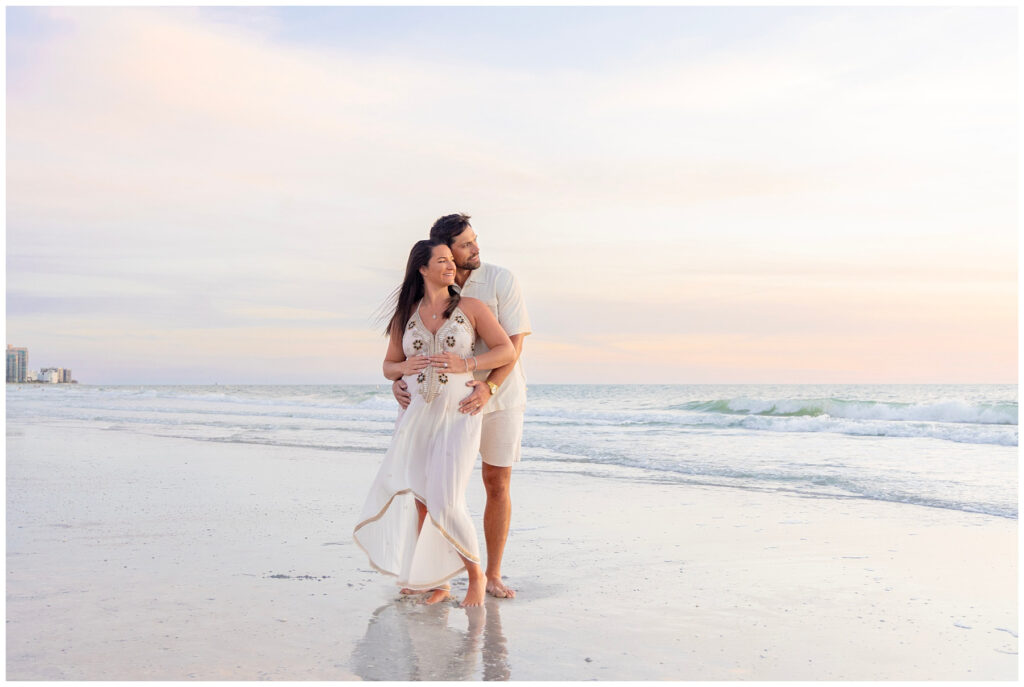 pregnant couple embracing on beach